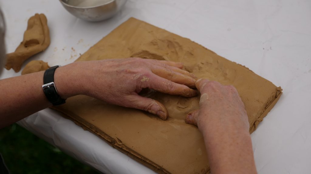 Zwei Hände modellieren eine flache Tontafel.